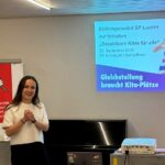 Anja Meier informiert zur Kitainitiative, im Hintergrund Präsentation und rote SP Fahne mit Rose und Schriftzug Solidarität